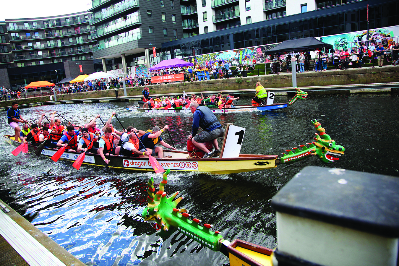 Two teams wearing lifejackets racing in dragon boats at Leeds Dock Southbank during the waterfront festival